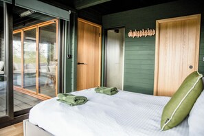 Un dormitorio con cama, almohada verde, puerta de madera y vistas por una puerta de cristal.