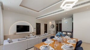 Een moderne eetruimte met een houten tafel gedekt voor zes personen, een ingebouwde televisie en een gezellige zithoek met een bank en stoelen.