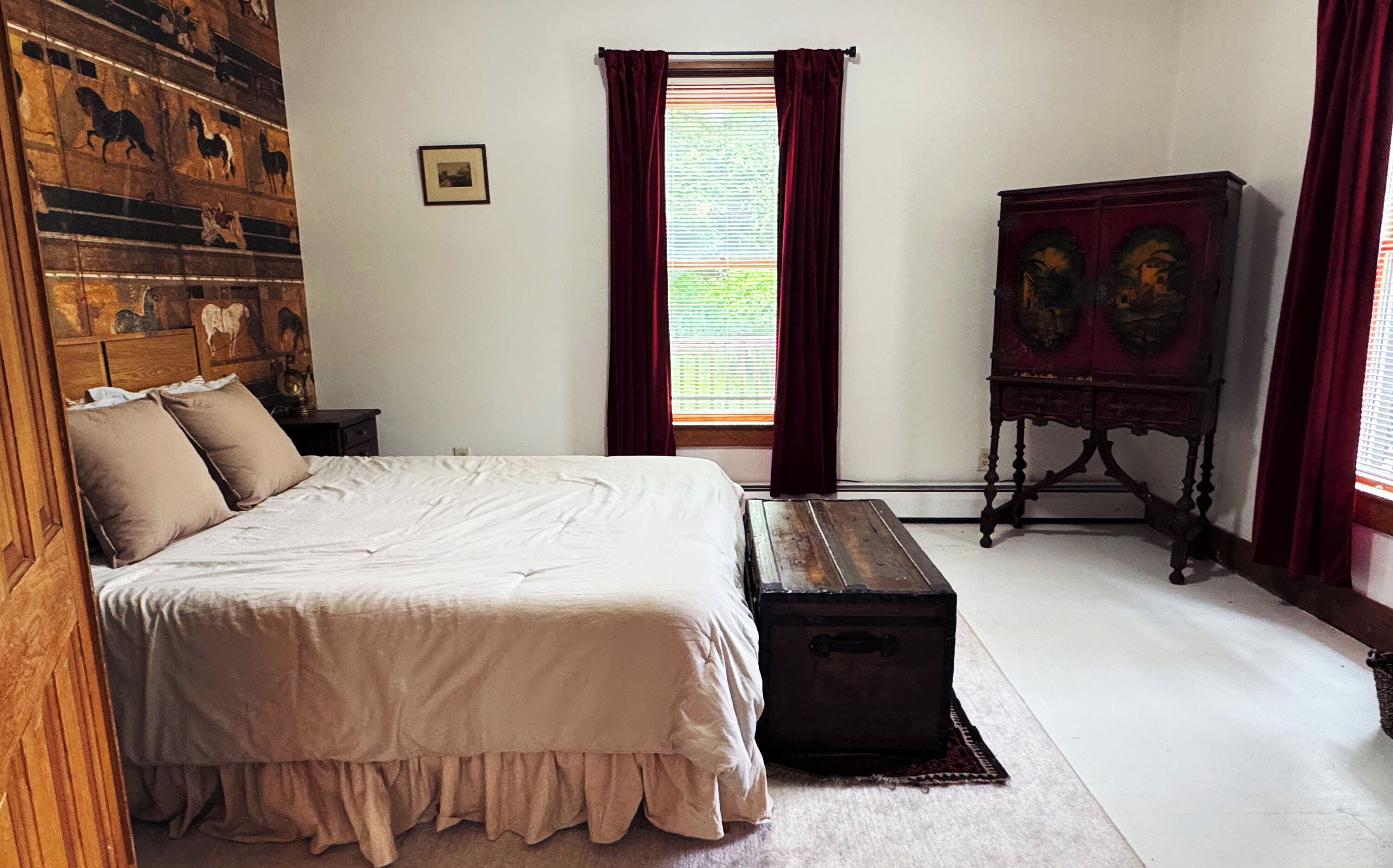 Een slaapkamer met een groot bed, een dressoir, een schilderij aan de muur en een raam met gordijnen.