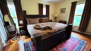 Un dormitorio con una cama grande, piso de madera y vistas a árboles por la ventana.