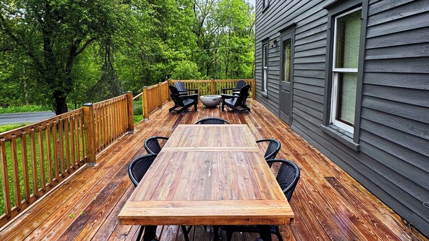 Una terraza de madera con una mesa y sillas, rodeada por una valla de madera, junto a un edificio con ventanas.