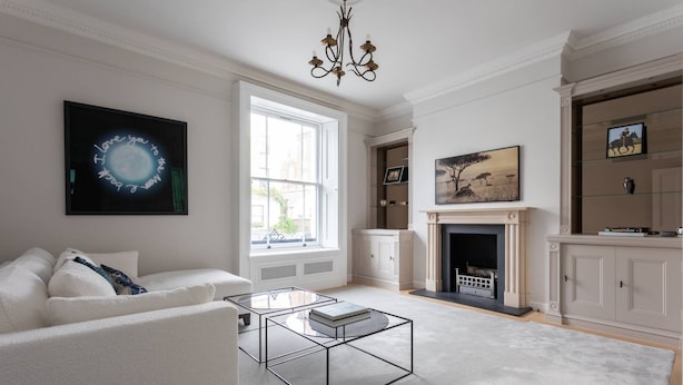 A spacious living room with a white sofa, a glass coffee table, a fireplace, and a large window providing natural light.
