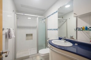 A modern bathroom with a glass-enclosed shower, a white toilet, and a sink with a blue countertop.