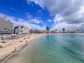 A beach with clear turquoise water, a sandy shore, and a row of hotels in the background.