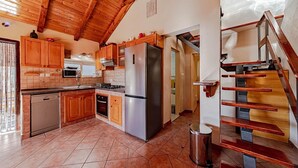 A kitchen with wooden cabinets, a stainless steel refrigerator, and a dishwasher. There is a staircase with wooden steps and metal railings.