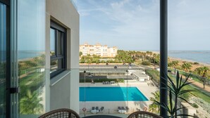 A balcony with a view of a swimming pool, a beach, and a hotel building.