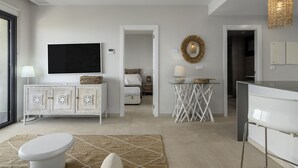 A modern living room with a flat-screen TV, a white cabinet, a dining area, and a kitchen.