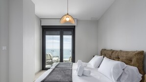 A modern hotel room with a large bed, a view of the sea through a sliding door, and a hanging pendant light.