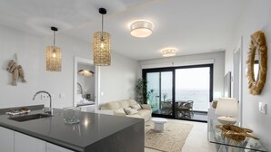 A modern kitchen with a central island, a dining area with a glass table, and a view of the sea through large windows.