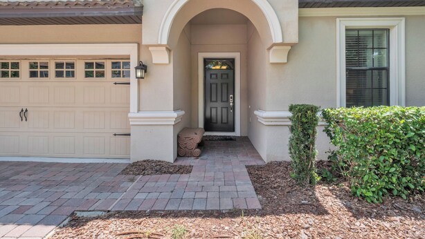 A house with a beige garage, a black front door, and a brick pathway leading to the entrance.
