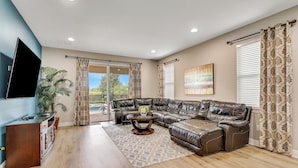 A modern living room with a leather sectional sofa, a flat-screen TV, a wooden coffee table, and a large potted plant. - 25% Off 10BR Encore Pool Villa Near DIsney (Kissimmee)