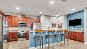 A modern kitchen with wooden cabinets, stainless steel appliances, a bar area with stools, and a flat-screen TV mounted on the wall. - 25% Off 10BR Encore Pool Villa Near DIsney (Kissimmee)