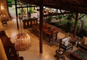 Um espaço de refeições interno com mobiliário de madeira, luminárias trançadas e vista para um jardim.