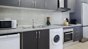 A modern kitchen with grey cabinetry, a built-in microwave, a sink, a washing machine, and a refrigerator. - Cubo's Casa Rural Fernando Family Fun / private pools / air conditioning / free Wi-Fi (Cártama)