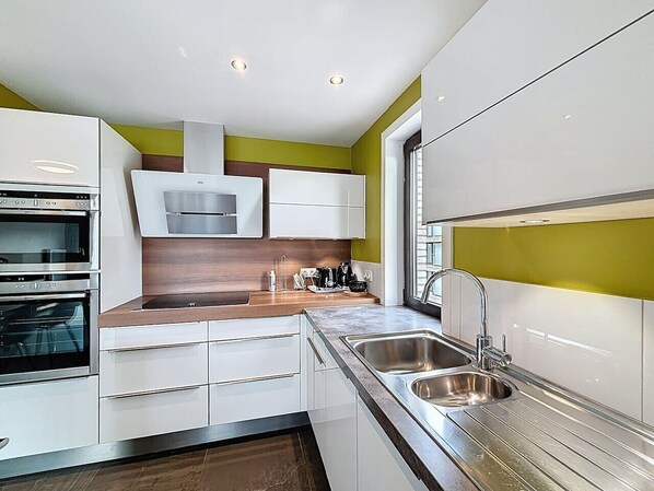 A modern kitchen with built-in appliances, a double sink, and a window providing natural light. - Flat Zandloper - Side sea view in Oostduinkerke (Koksijde)
