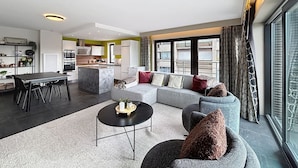 A modern living room with a grey sofa, a black coffee table, and a dining area with a table and chairs. - Flat Zandloper - Side sea view in Oostduinkerke (Koksijde)