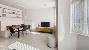 A modern living room with a dining area, a TV, and a large window with curtains.
