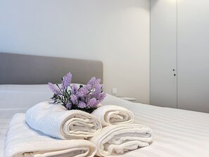 A neatly made bed with rolled white towels and a small purple flower arrangement. - Flat Hannah - center of De Panne (De Panne)