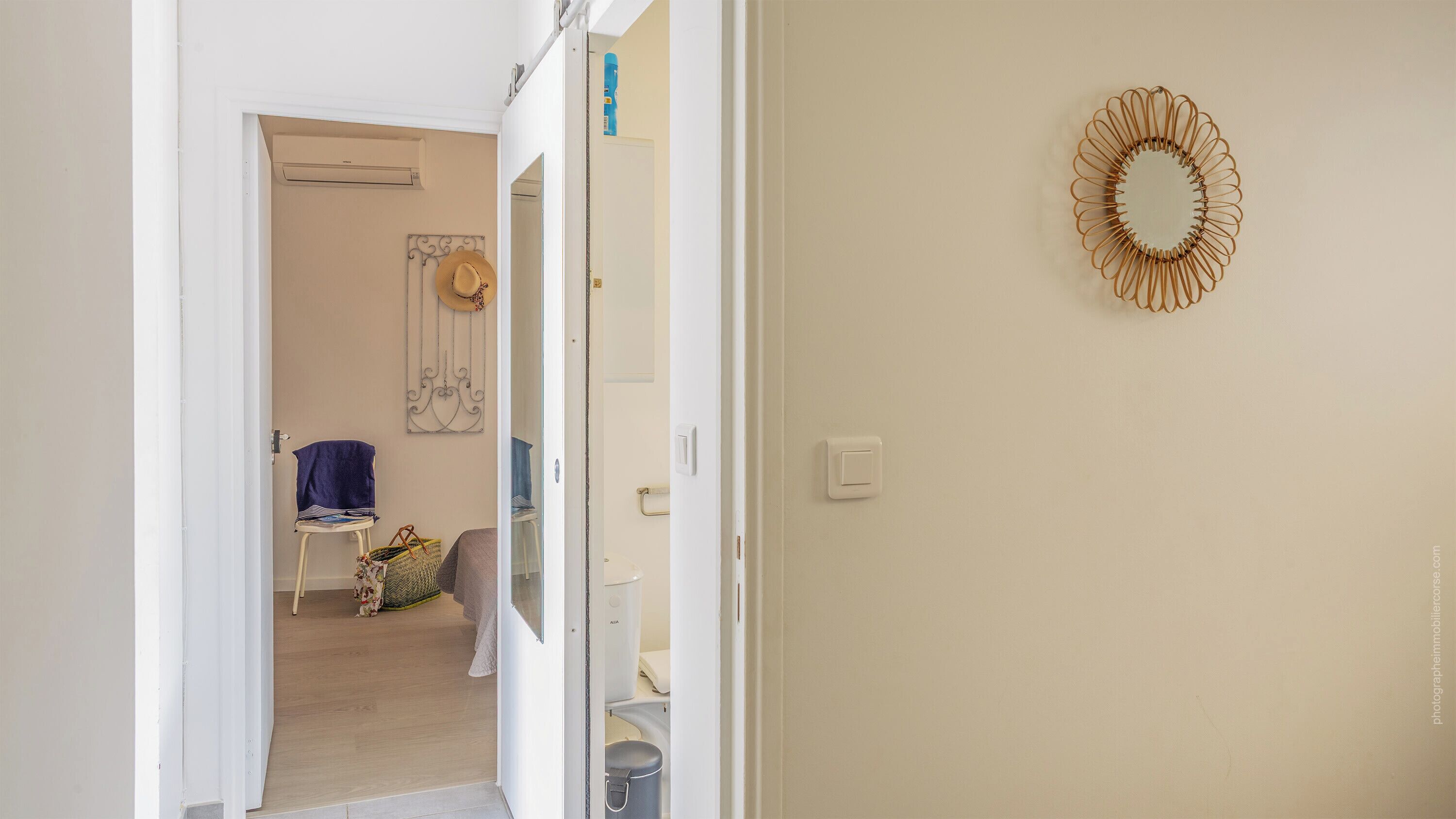 A hallway leading to a bathroom with a towel rack, a hat, and a decorative mirror.
