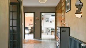 Un pasillo con un radiador, una puerta con paneles de vidrio esmerilado y una lámpara fijada a la pared.