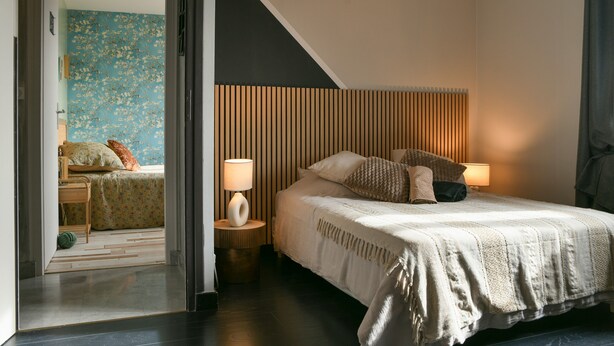 Un dormitorio con cama, dos lámparas de noche, cabecera de madera y vista a otra habitación.