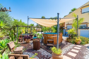 A patio area with a hot tub, wooden furniture, and potted plants.