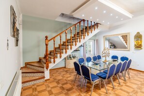 A dining area with a glass table and blue chairs, a staircase with wooden balusters, and a Buddha statue on the wall.