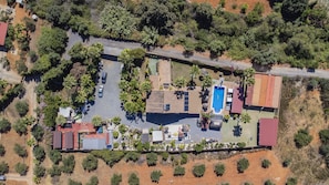 Vue aérienne d’une propriété dotée d’une piscine, d’un patio couvert et d’un bâtiment au toit rouge.