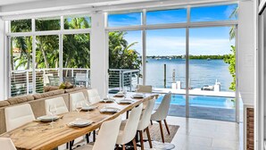 A modern dining area with a view of the water, large windows, and a pool. - Miami Stunning Waterfront Villa Escape (North Bay Village)
