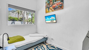 A bedroom with a bed, a window, a painting, a TV, and a view of buildings and palm trees. - Miami Stunning Waterfront Villa Escape (North Bay Village)