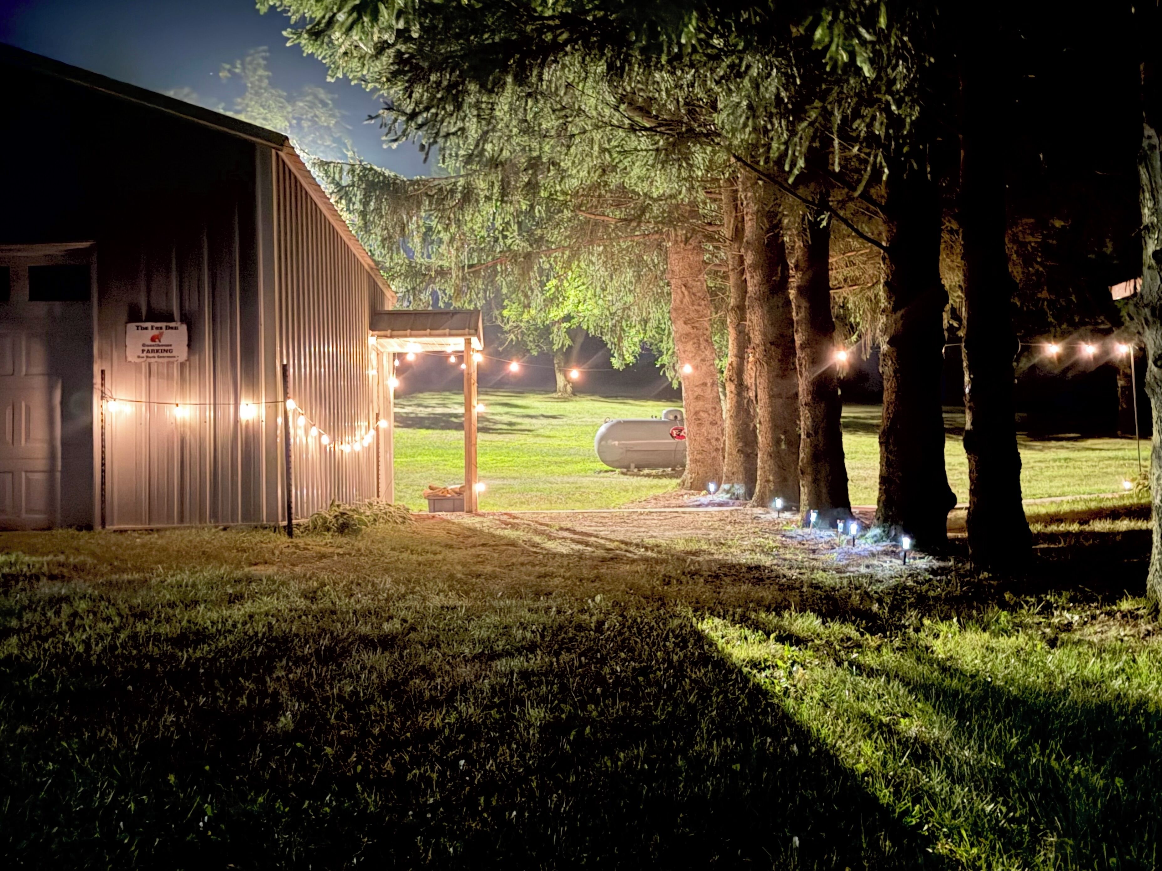 A building with a sign indicating it is a parking area, surrounded by trees and illuminated by string lights.