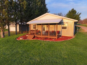 A small wooden cabin with a porch, a garage, and a well-maintained lawn.