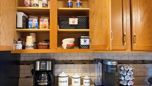 Une cuisine avec des meubles de rangement en bois, une machine à café, des récipients pour le thé et le sucre, et un distributeur de grains de café.