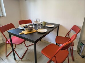 Una mesa de comedor con cuatro sillas rojas, un cuenco de aceitunas, un vaso de agua y una taza verde.