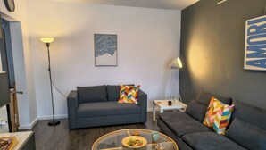 A modern living room with a grey sofa, a round glass coffee table, and a small white side table with a lamp. - Student Grey Apartment w/ Full ammenities. Spacious 2 room Balcony (Timisoara)