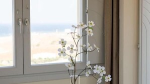 Ein Essbereich mit Tisch und Stühlen, einer Blumenvase und Blick auf den Strand durch ein Fenster.
