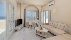 Ein modernes Wohnzimmer mit Fernseher, einer Couch, einem Esstisch mit Stühlen und Blick auf den Strand durch große Fenster.