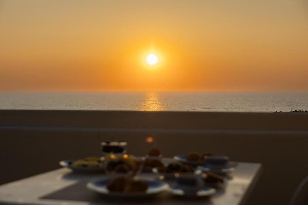Una mesa dispuesta con platos de comida y una vista del atardecer sobre el océano.