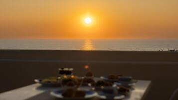 Una mesa dispuesta con platos de comida y una vista del atardecer sobre el océano.
