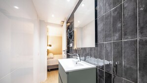 Un baño moderno con un espejo grande, paredes de azulejos oscuros y un lavamanos blanco.