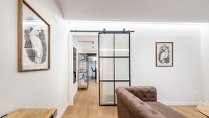 Una sala de estar moderna con un puerta corrediza de vidrio que da a un comedor, un sofá marrón y cuadros en las paredes.