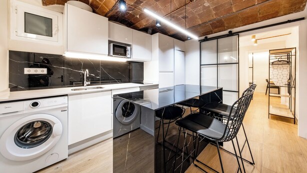 Una cocina moderna con lavadora integrada, microondas y comedor con mesa y sillas.