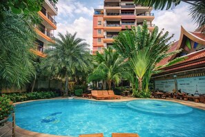 Una piscina rodeada de palmeras y sillas de descanso, con un edificio de varios pisos al fondo.