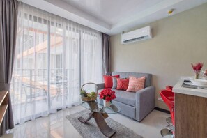 Un salon moderne avec un canapé gris, des coussins rouges, une table basse en verre et un balcon offrant une vue dégagée.