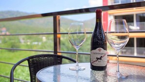 A bottle of wine and two glasses on a table with a view of mountains and a building in the background. - Nara Condo 1br | Pool view | nbc nai harn (Rawai)