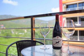 A bottle of wine and two glasses on a table with a view of mountains and a building in the background. - Nara Condo 1br | Pool view | nbc nai harn (Rawai)
