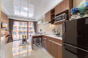 A modern kitchen with a large window, stainless steel appliances, and a dining area with bar stools. - Nara Condo 1br | Pool view | nbc nai harn (Rawai)