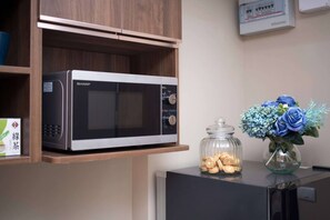 Un horno microondas en un estante, un tarro de cristal con galletas y un florero con flores.