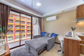 Ein modernes Zimmer mit Schlafsofa, kleinem Tisch, Spüle und Fenster mit Blick auf ein Gebäude mit orange-weißen Streifen.