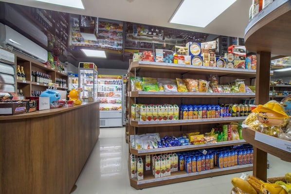 Interior de una tienda de comestibles con estantes llenos de diversos productos, una sección refrigerada y un mostrador con aperitivos.